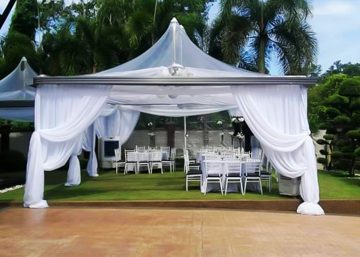 A large white tent rental set up in a backyard setting with pre-set furniture and equipment.